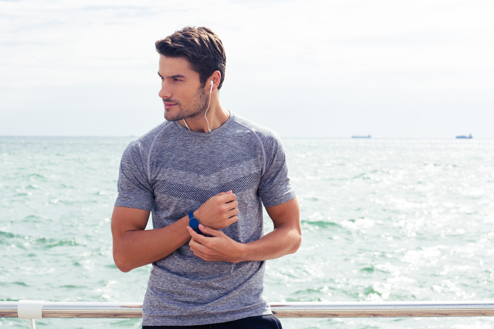 Portrait of a happy sports man standing near sea outdoors